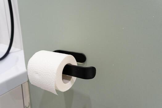 In an organized and wellarranged bathroom, a sleek black holder elegantly displays a single roll of toilet paper, ensuring that it is easily accessible for immediate use whenever needed photo