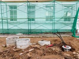A construction site featuring scaffolding and concrete rings embedded in the earth, surrounded by various materials and elements related to building and landscaping activities photo