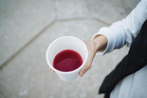 A person nonchalantly holds a cup filled with a vibrant, eyecatching red liquid, which beautifully highlights the vivid contents of the cup in contrast to the surrounding environment photo