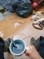 POV of hands of person holding a coffee cup front a inundation with mud and garbage. photo