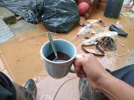 POV of hands of person holding a coffee cup front a inundation with mud and garbage. photo