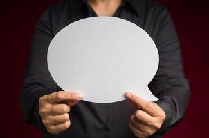Text speech bubble concept. Close-up of hand holding a white speech bubble against a red background photo