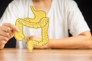 Hand holding a large intestine shape made from paper while sitting over a black background photo