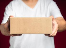 Man in white casual holding a cardboard box while standing on a red background photo