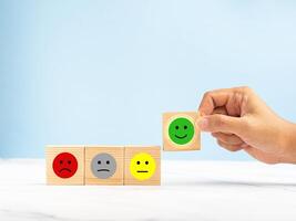Hand holding a wooden cube with the happy smiley face icon to give the best satisfaction to the service photo