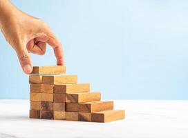 Close-up of hand holding a wooden block arranging to stack for development as step stair on a marble floor over a blue background photo