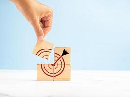 Close-up of hand holding a wooden cube with a target icon over a marble floor against a blue background photo
