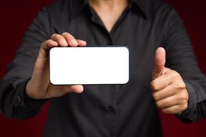 Hand holding a horizontal mobile phone with a blank white screen and showing thumbs up while standing on a red background photo