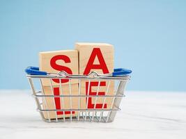 A miniature shopping trolley and wooden blocks with the word SALE on a blue background photo