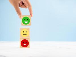 Hand holding a wooden cube with the happy smiley face icon to give the best satisfaction to the service photo