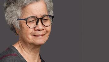 Senior woman with short gray hair looking down with a smile while standing on gray background photo