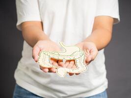 Hand holding a large intestine shape made from yellow paper in palm while standing over a gray background photo