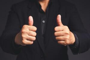 Businessman in a suit shows thumbs up with both hands while standing on gray background in the office photo