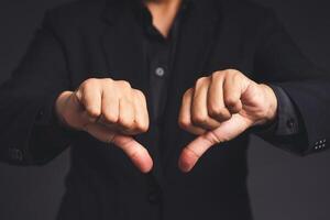 Negative concept. Close-up of businessman hands in a black suit showing thumbs down while standing on a gray background photo