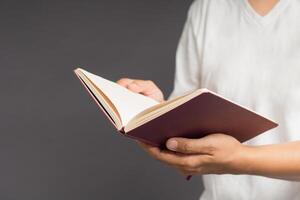 Close-up of man in white casual holding a book while standing on a gray background photo