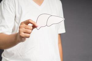 Hand holding a liver shape made of paper while standing on a gray background photo