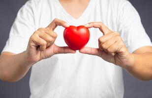 Close-up of hand holding a red heart shape while standing on a gray background photo