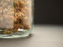 Dry cannabis buds flower in a jar glass on the table with a black background photo