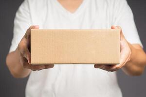 Man in white casual holding a cardboard box while standing on a gray background photo
