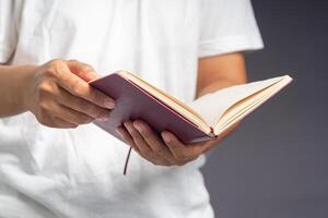 Close-up of man in white casual holding a book while standing on a gray background photo