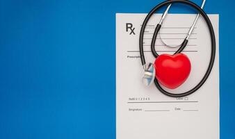 Top view of a stethoscope and a red heart shape over the medical prescription sheet on a blue background photo