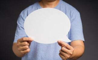 Hand holding a white speech bubble against a gray background while standing in the studio photo
