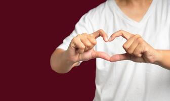 Man in white casual making heart figure love sign with fingers while standing on a red background photo