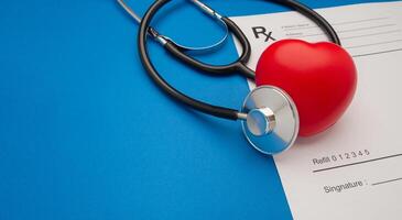 Top view of a stethoscope and a red heart shape over the medical prescription sheet on a blue background photo