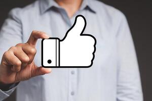Close-up of hand holding a thumbs up a symbol while standing on a gray background photo