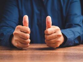Businessman showing thumbs up with both hands while sitting at the table in the office photo