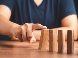 Risk and strategy in business concept. Close-up of hand pushing a wooden block on a line of dominos while sitting in the office photo