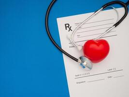 Top view of a stethoscope and a red heart shape over the medical prescription sheet on a blue background photo