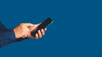 Close-up of hands using a mobile phone while standing over a blue background photo