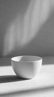 A white bowl sits on a table in front of a window photo