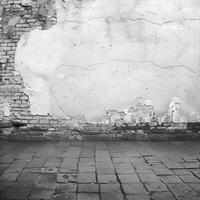 Weathered Brick Wall with Cracked Plaster and Cobblestone Ground in Black and White Urban Setting photo