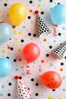 Colorful Party Balloons and Polka Dot Party Hats on a Confetti Background photo