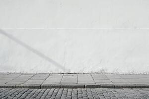 Minimalist Urban Street Scene with Sunlit White Wall and Cobblestone Sidewalk in Daylight photo