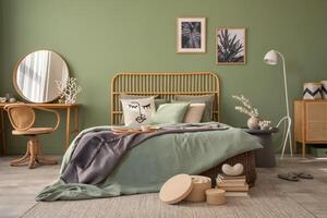 Stylish bedroom interior design with mock up poster frames, bed, side table, rattan commode, vanity table and creative home accessories. Sage green wall. Template. Copy space. photo