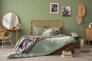Stylish bedroom interior design with mock up poster frames, bed, side table, rattan commode, vanity table and creative home accessories. Sage green wall. Template. Copy space. photo
