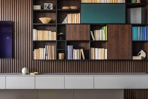 Modern bookcase in lamells wall. Grey chest of drawers. Bookcase a lot of books and accessories. Herringbone wooden parquet. Cat in open spaces. photo