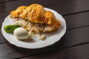 Croissant sandwich with tuna, egg, cucumber and cheese on a white plate photo