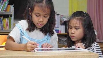 Sister teaching younger sister to touch digital tablet screen on table using stylus pen, design ideas, coloring on online learning app at home. video