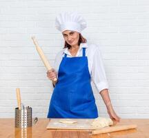 portrait of mature woman in cook uniform with rolling pin and dough photo
