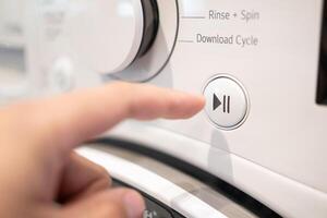 A finger pressing the start button on a washing machine. Close up view of automatic washing machine. photo