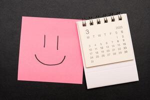 Simple desk calendar for MARCH 2025 with smiling face on sticky note. Calendar concept with copy space. 2025 MAR calendar. photo