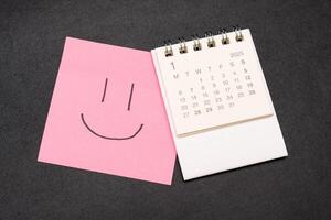Simple desk calendar for JANUARY 2025 with smiling face on sticky note. Calendar concept with copy space. 2025 JAN calendar. photo