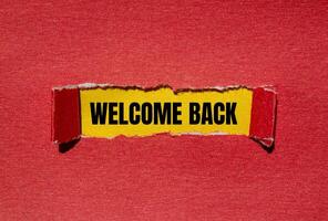 Welcome back message written on ripped torn red paper with yellow background. Conceptual welcome back symbol. Copy space. photo