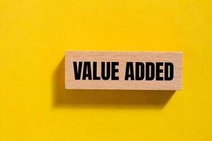 Value added message written on wooden block with yellow background. Conceptual value added symbol. Copy space. photo