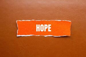 Hope message written on ripped orange torn paper piece with brown background. Conceptual hope symbol. Copy space. photo