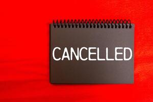Cancelled message written on black notebook page with red background. Conceptual cancelled symbol. Copy space. photo